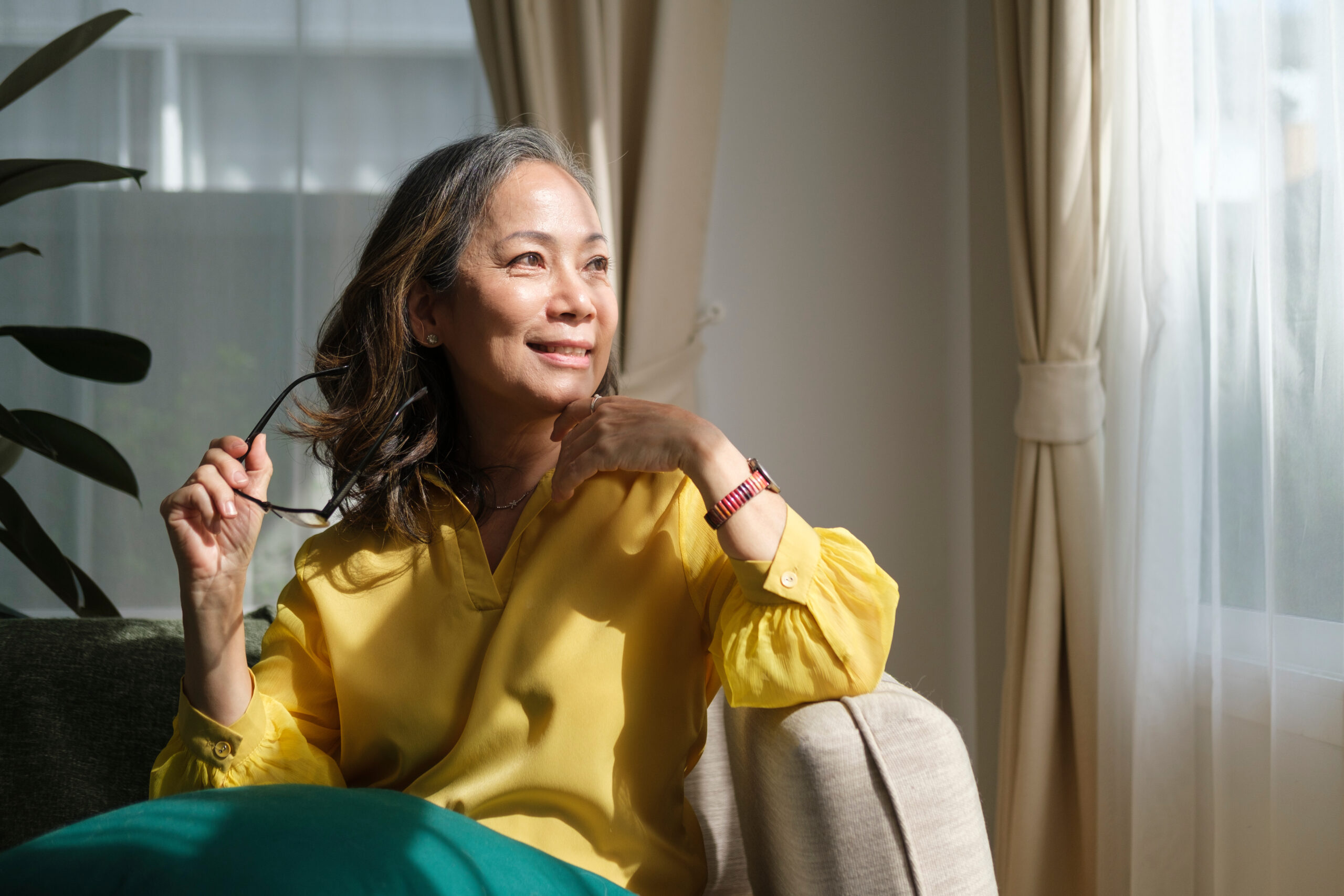 Middle aged woman resting on comfortable couch, looking away thinking dreaming enjoy stress free peaceful mood wellbeing alone in living room.