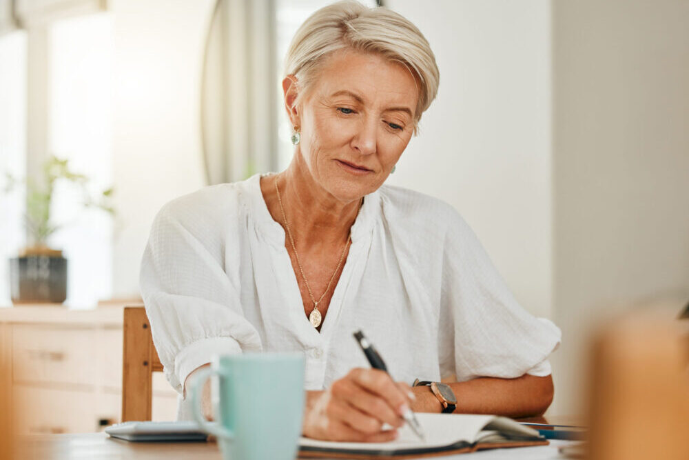 Writing, thinking and senior woman at a house making notes on notebook paper. Retirement of a serious person from Sweden think about schedule, day agenda idea or document and write ideas at home